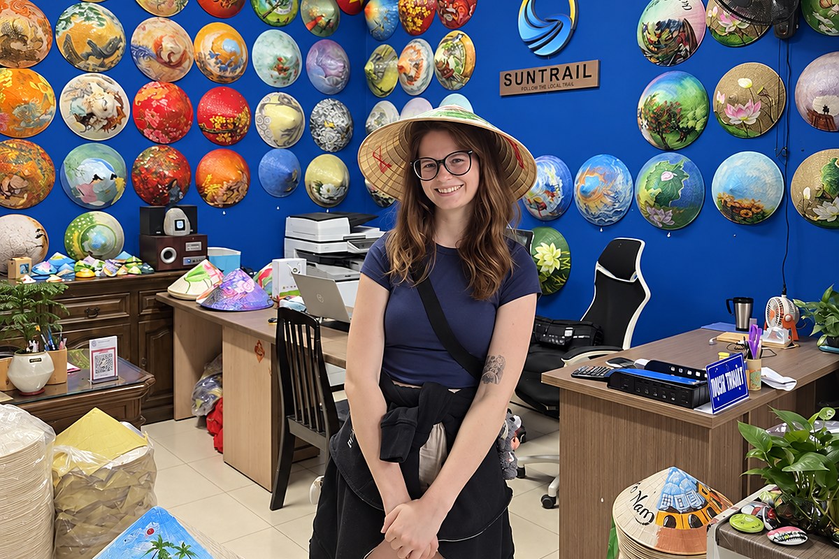 Tourist wearing a hand-painted conical hat in front of a wall of painted Vietnamese nón lá in Ho Chi Minh City